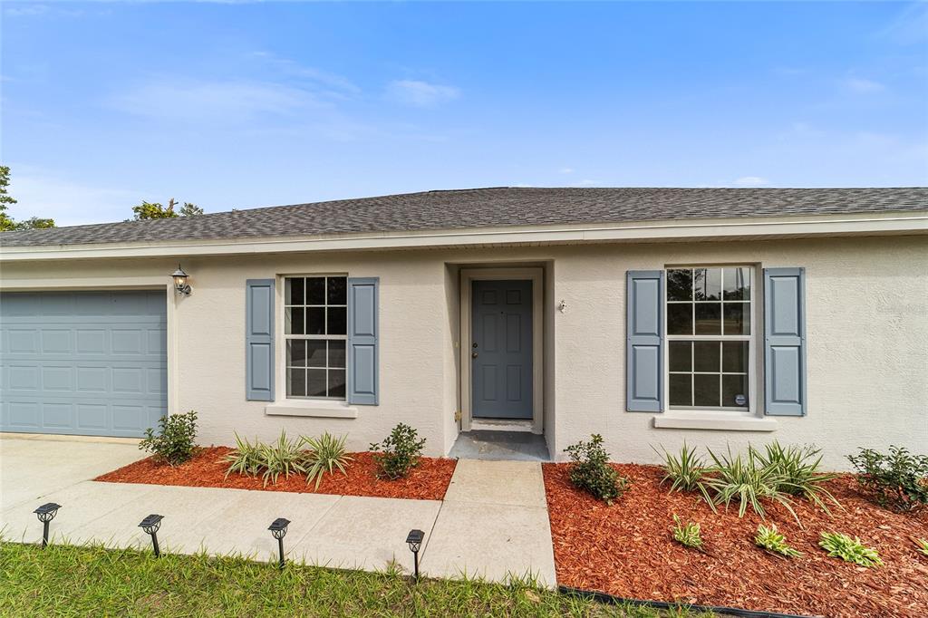 A single-story house exterior features a gray garage door, blue shutters, and a front entrance — 13029 SW 35TH AVENUE ROAD, OCALA, FL