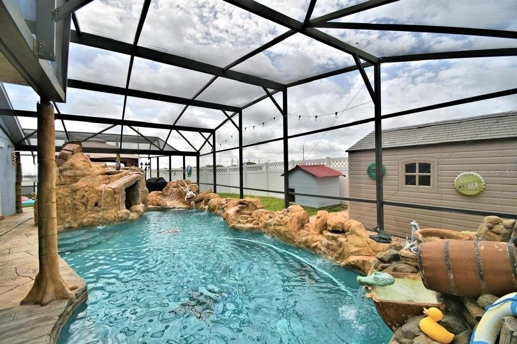 A screened-in swimming pool features rock waterfalls, a decorative barrel, and a small storage shed — 260 CHESHIRE WAY, DAVENPORT, FL