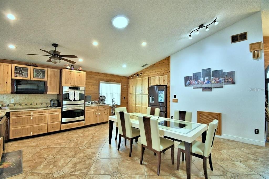 A kitchen and dining area with light wood cabinets, tile flooring, and a vaulted ceiling — 260 CHESHIRE WAY, DAVENPORT, FL