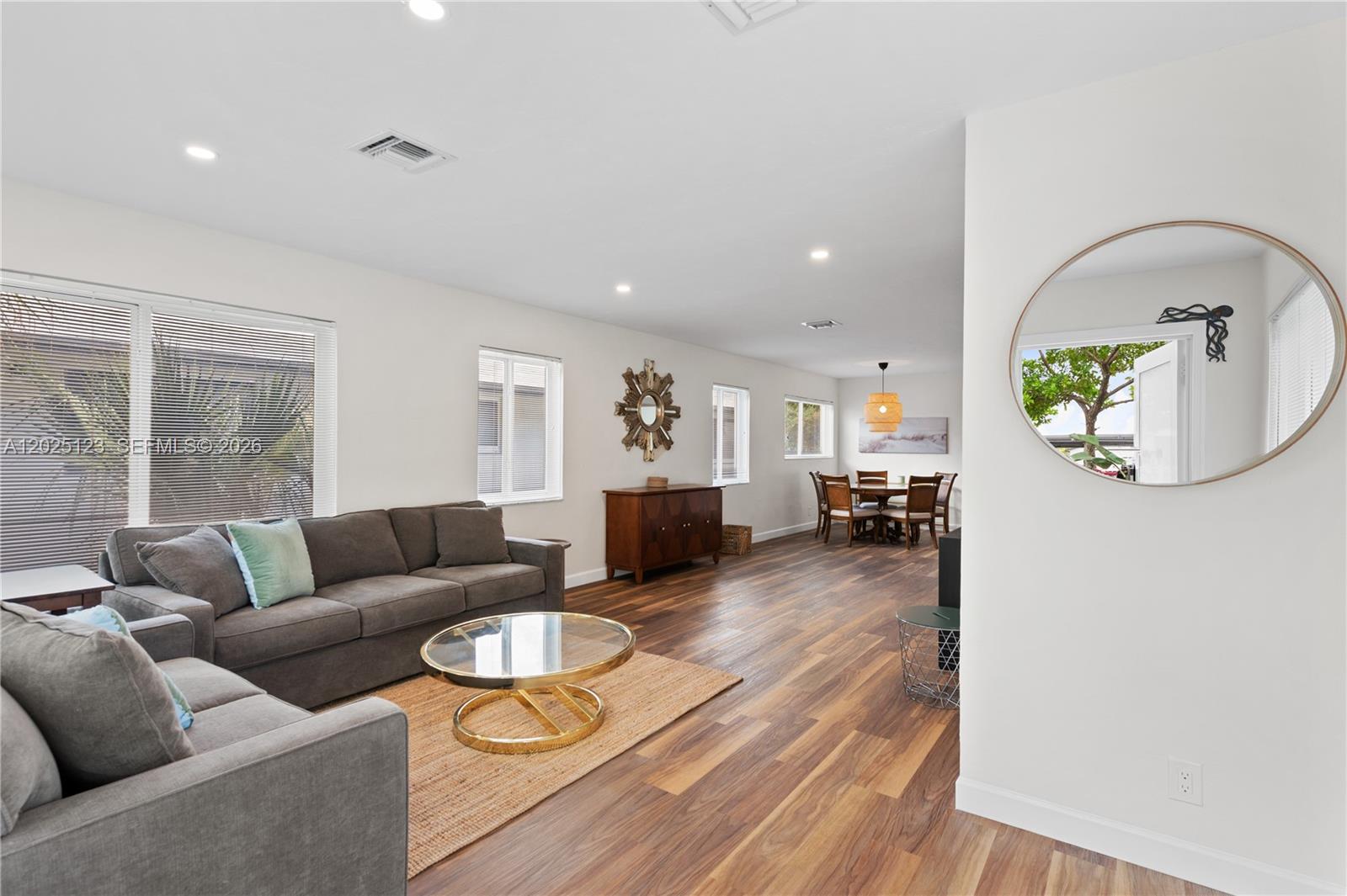 An open-concept living and dining area features wood-look flooring, a gray sofa, and a mirror — 1715 Jefferson St # 0, Hollywood FL 33020, HOLLYWOOD, FL