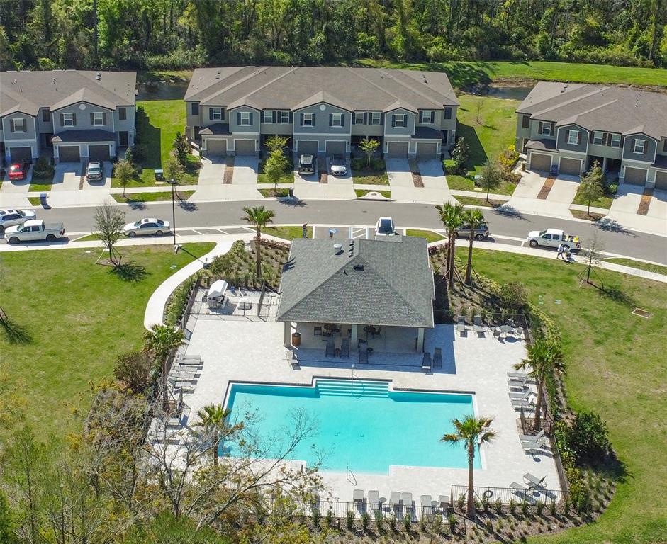 An aerial view shows a community swimming pool and clubhouse surrounded by residential townhomes — 17616 NECTAR FLUME DRIVE, LAND O LAKES, FL