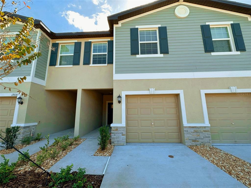 The exterior of a two-story townhouse features tan stucco, green siding, and two garage doors — 17616 NECTAR FLUME DRIVE, LAND O LAKES, FL
