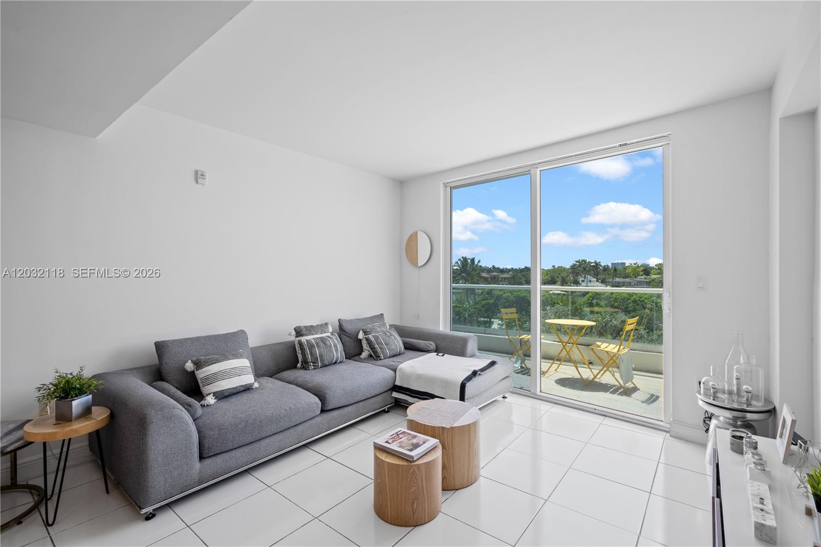 A living room features a gray sectional sofa, wooden side tables, and a balcony view — 6362 Collins Ave # 312, Miami Beach FL 33141, MIAMI BEACH, FL