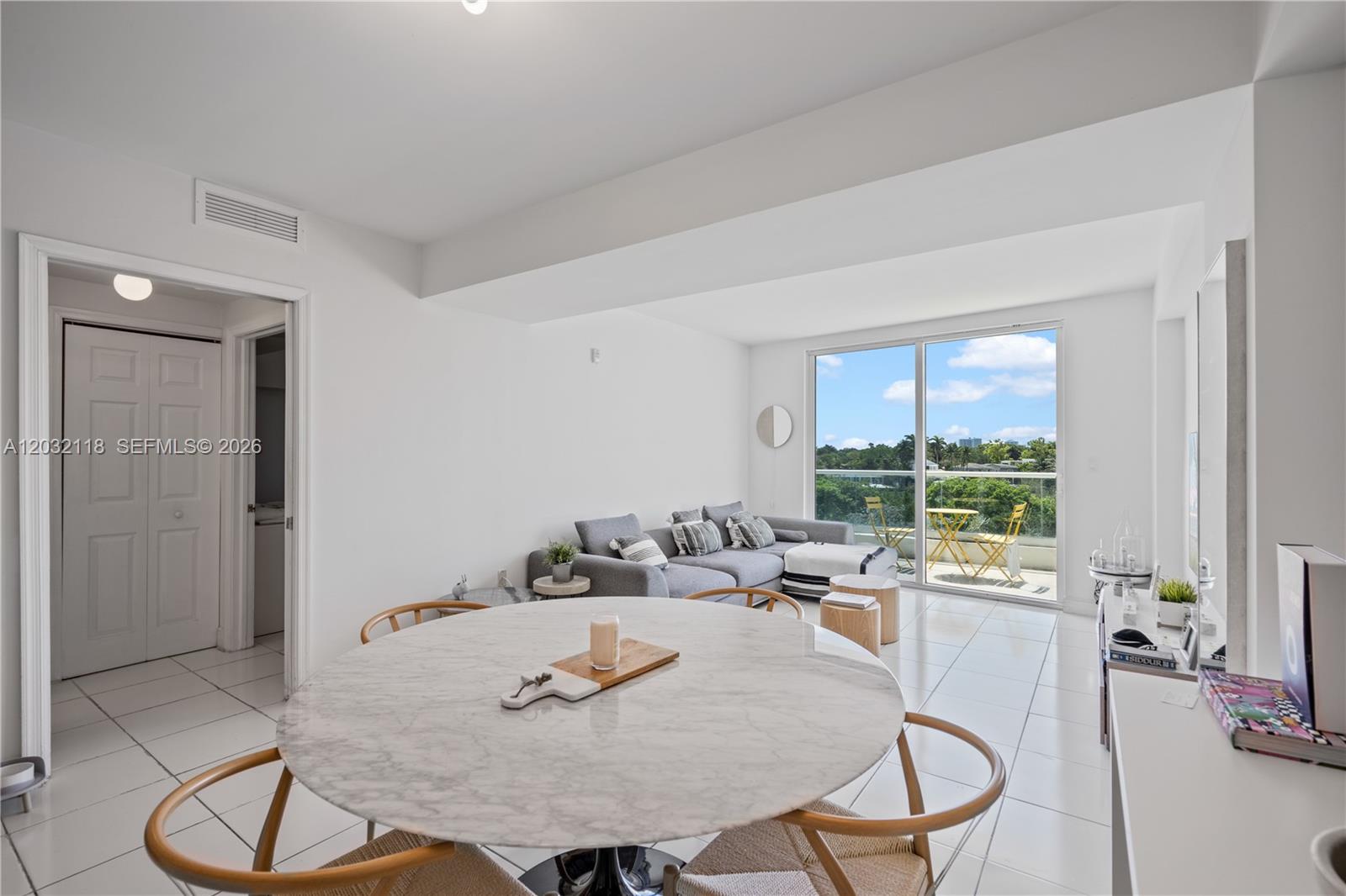 A bright living and dining area features white tile floors, a marble table, and balcony — 6362 Collins Ave # 312, Miami Beach FL 33141, MIAMI BEACH, FL