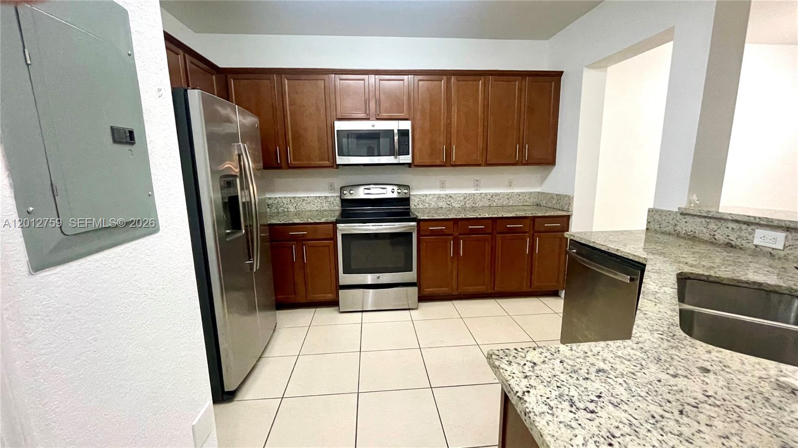A kitchen features wood cabinets, stainless steel appliances, and granite countertops over tile flooring — 10620 NW 88th St # 205, Doral FL 33178, DORAL, FL