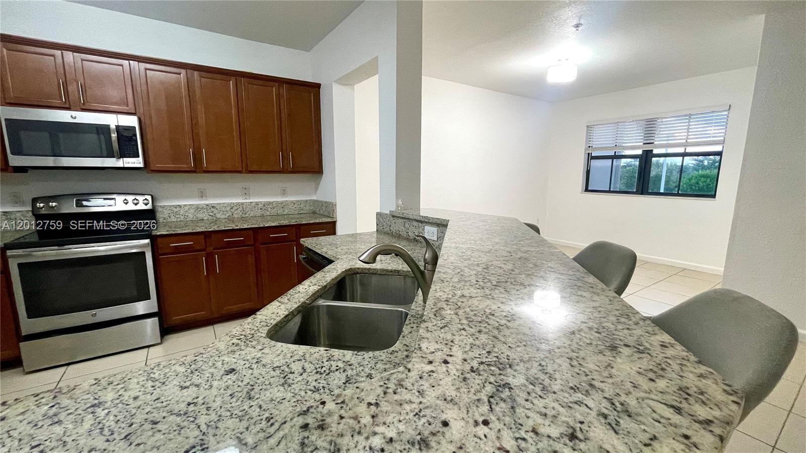 A kitchen features wood cabinets, granite countertops, stainless steel appliances, and a breakfast bar — 10620 NW 88th St # 205, Doral FL 33178, DORAL, FL