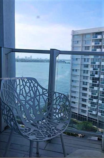 A balcony with a modern patterned chair overlooks a bay and a high-rise building — 1100 West Ave # 517, Miami Beach FL 33139, MIAMI BEACH, FL