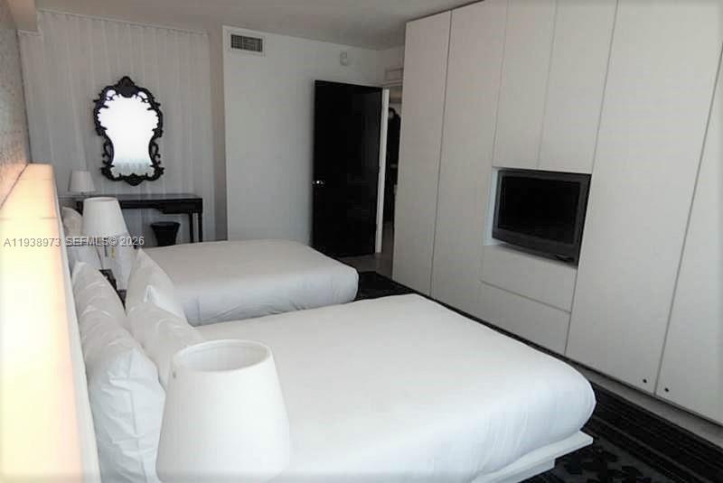 A bedroom features two white beds, a built-in wall unit with a television, and a mirror — 1100 West Ave # 517, Miami Beach FL 33139, MIAMI BEACH, FL