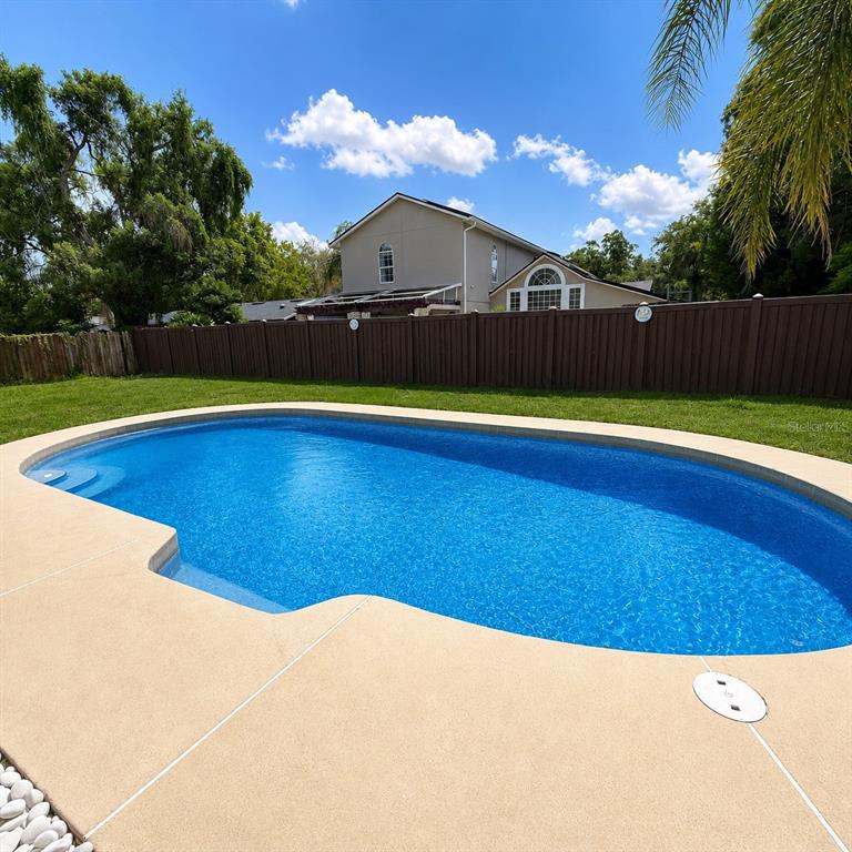 A backyard features a blue swimming pool with a tan concrete deck and brown fence — 641 BROOKSIDE ROAD, MAITLAND, FL