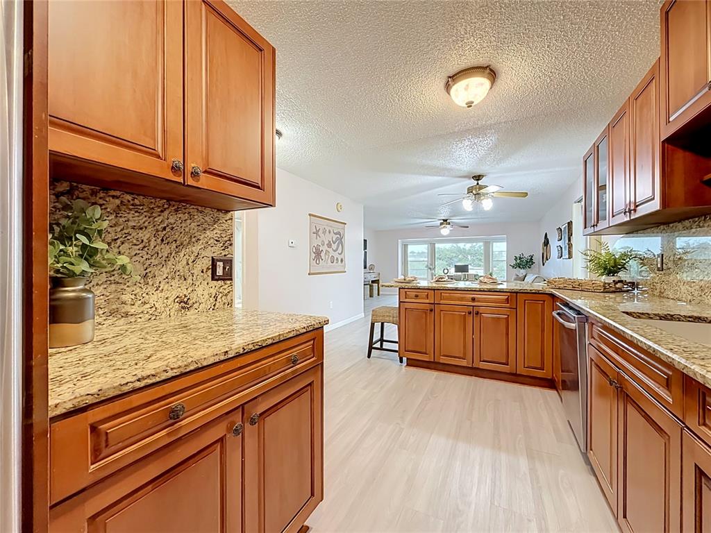 A kitchen with wood cabinets, granite countertops, and light flooring opens into a living area — 1900 68TH STREET N UNIT 301, ST PETERSBURG, FL