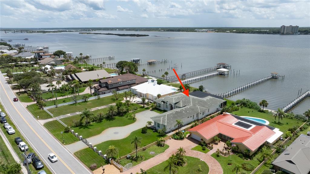 An aerial view shows waterfront homes with docks, swimming pools, and a road along the coast — 3020 S PENINSULA DRIVE, DAYTONA BEACH SHORES, FL