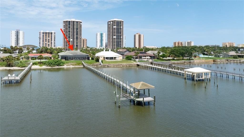 An aerial view shows a waterfront house with a long dock extending into the bay — 3020 S PENINSULA DRIVE, DAYTONA BEACH SHORES, FL