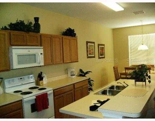 A kitchen features light-colored countertops, wooden cabinets, a white stove, and an island with a sink — 622 ALFANI STREET, DAVENPORT, FL