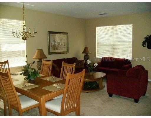 A dining area with a wooden table and chairs sits adjacent to a carpeted living room — 622 ALFANI STREET, DAVENPORT, FL