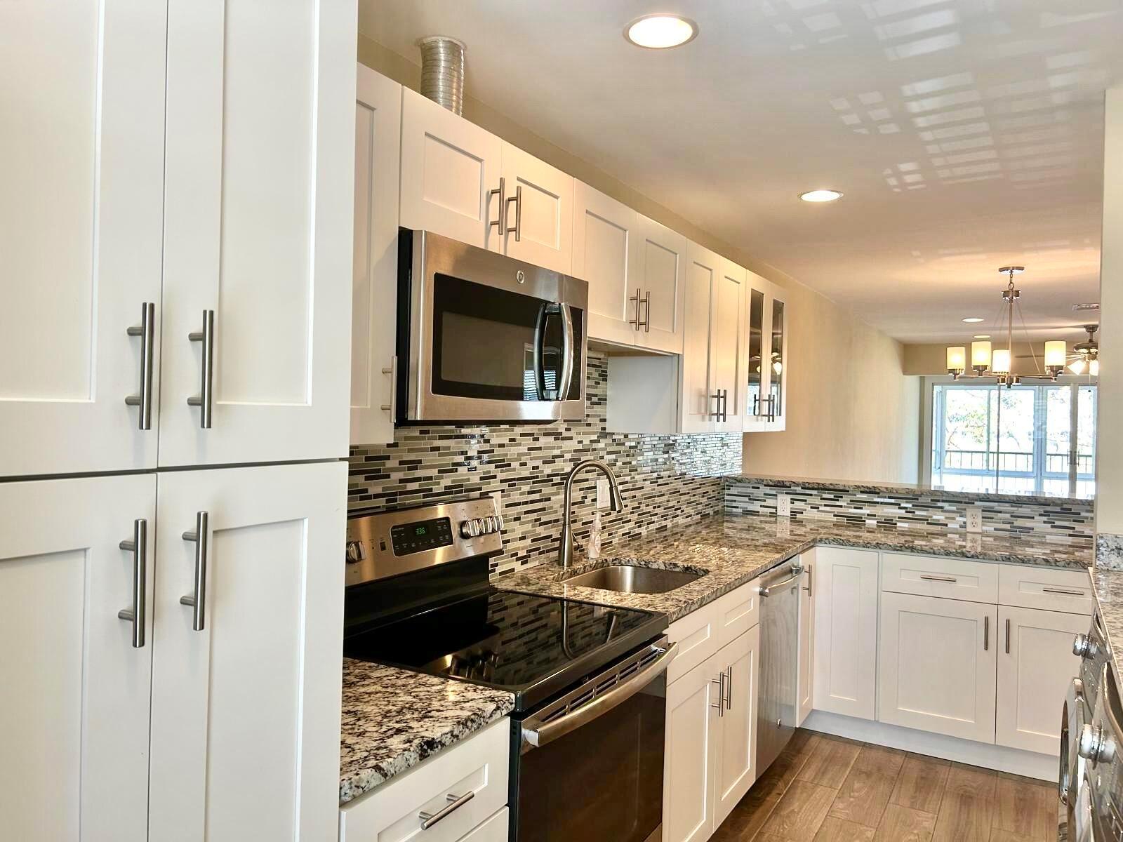 A kitchen with white cabinets, granite countertops, stainless steel appliances, and a mosaic tile backsplash — 2811 SW 15th Street # 202, Delray Beach FL 33445, DELRAY BEACH, FL