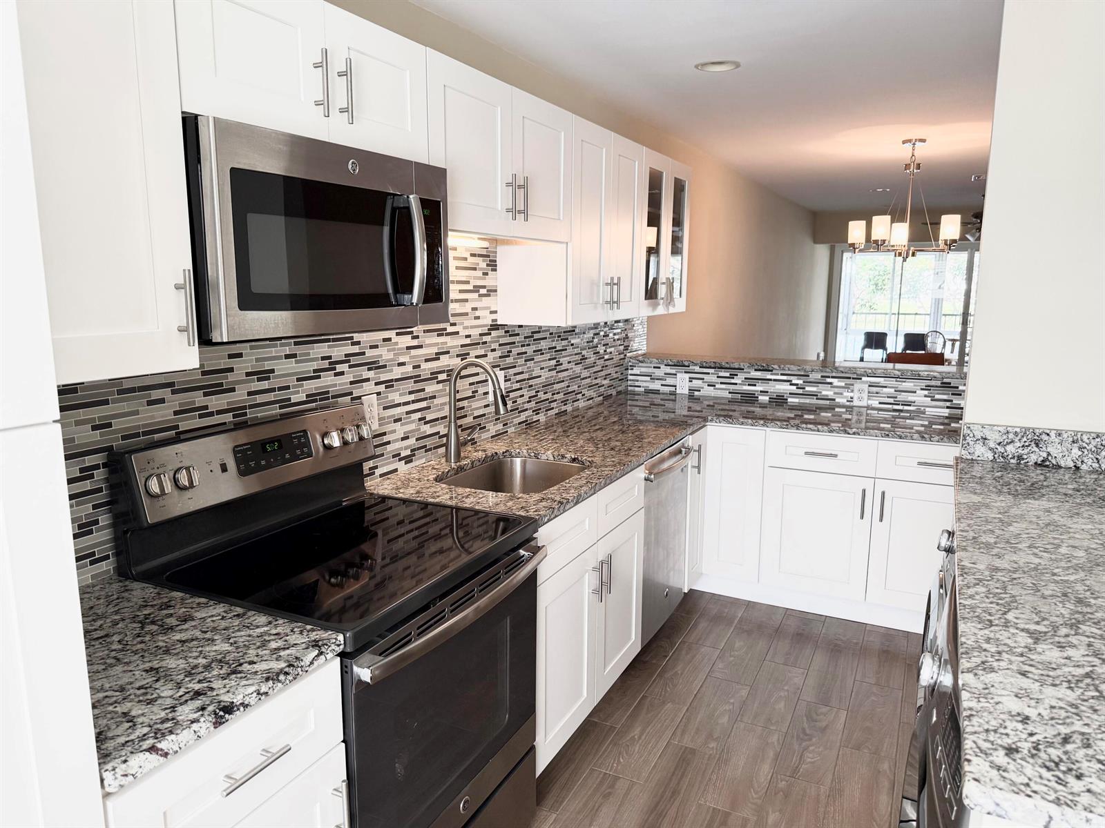A kitchen features white cabinets, granite countertops, stainless steel appliances, and a mosaic tile backsplash — 2811 SW 15th Street # 202, Delray Beach FL 33445, DELRAY BEACH, FL