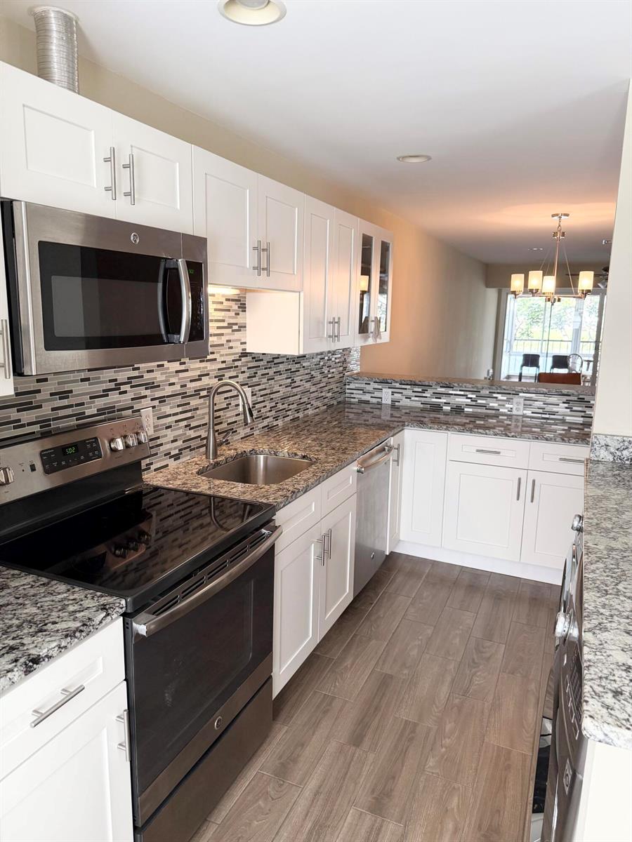 A kitchen features white cabinets, granite countertops, stainless steel appliances, and a mosaic tile backsplash — 2811 SW 15th Street # 202, Delray Beach FL 33445, DELRAY BEACH, FL