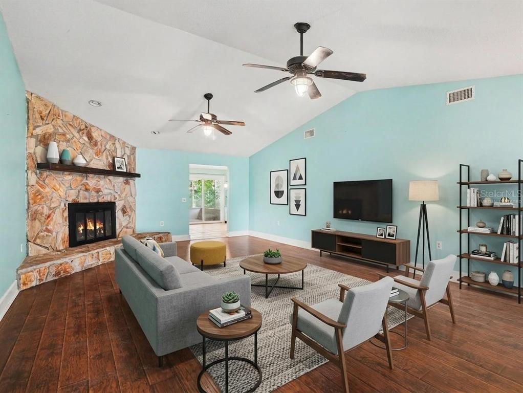 A living room features a stone fireplace, light blue walls, vaulted ceilings, and wood flooring — 928 TIMBERGREEN DRIVE, LAKELAND, FL