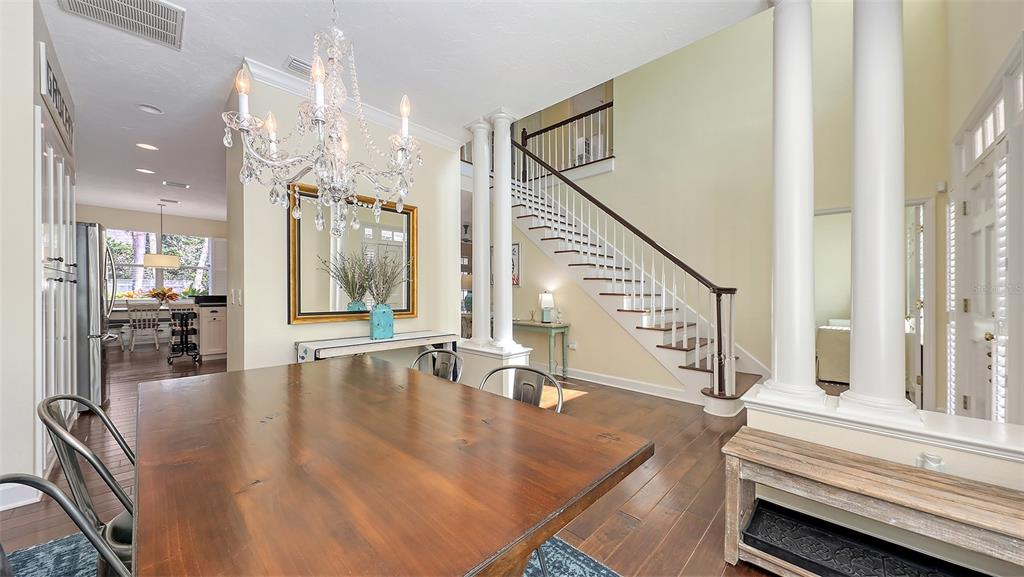 A dining area features a wooden table, crystal chandelier, and a staircase with white columns — 1105 92ND STREET NW, BRADENTON, FL