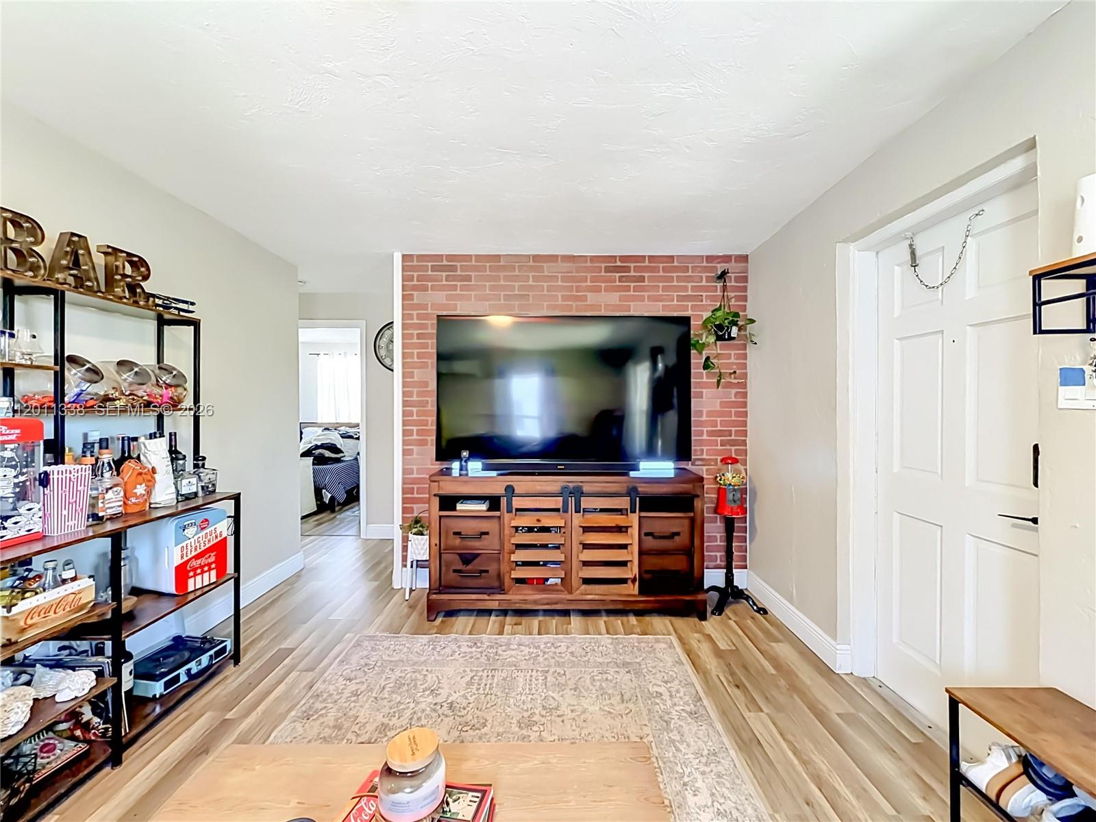 A living room features a brick accent wall, a wooden media console, and a bar shelf — 800 NW 17th Ter, Pompano Beach FL 33069, POMPANO BEACH, FL