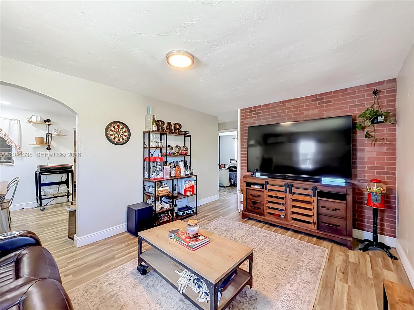 A living room features a brick accent wall, a large television, and a bar shelf — 800 NW 17th Ter, Pompano Beach FL 33069, POMPANO BEACH, FL