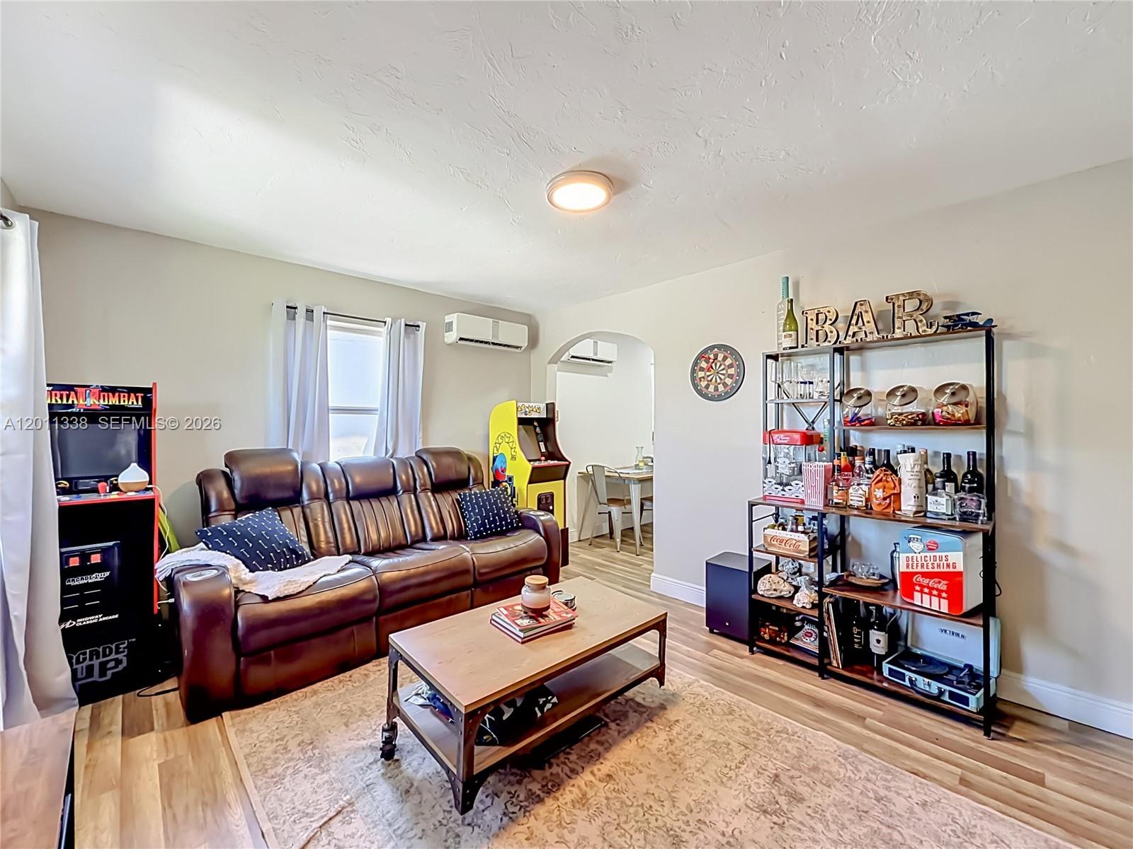 A living room features a leather sofa, arcade games, a bar shelf, and wood flooring — 800 NW 17th Ter, Pompano Beach FL 33069, POMPANO BEACH, FL