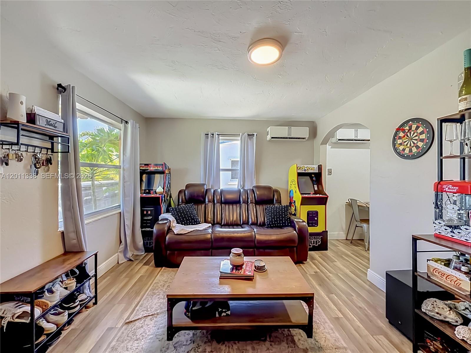 A living room features a brown leather sofa, two arcade cabinets, and wood-look flooring — 800 NW 17th Ter, Pompano Beach FL 33069, POMPANO BEACH, FL