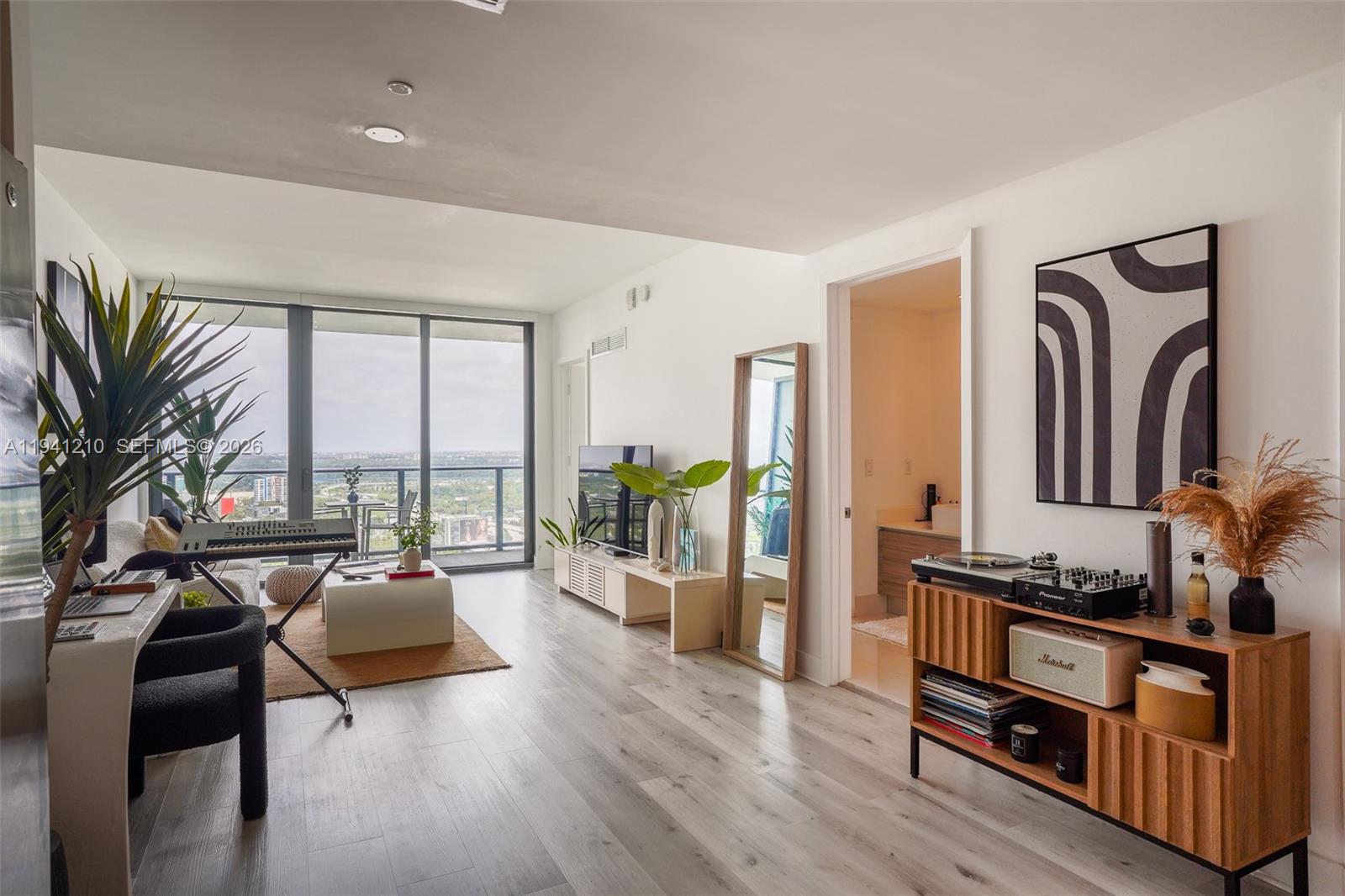 A modern living room features light wood floors, a balcony with city views, and musical equipment — 121 NE 34th St # 2711, Miami FL 33137, MIAMI, FL
