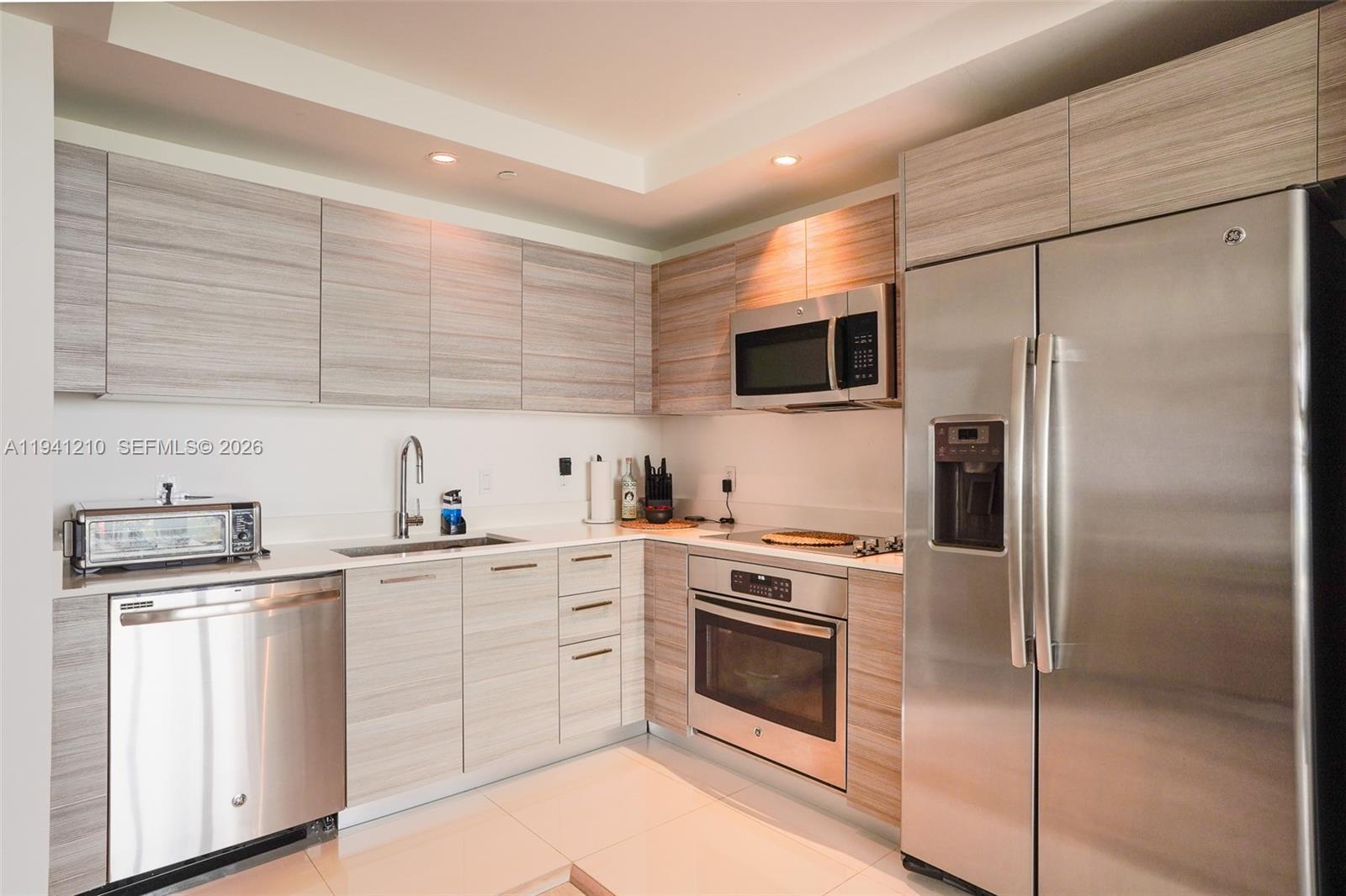 A modern kitchen features light wood-grain cabinetry, stainless steel appliances, and white countertops — 121 NE 34th St # 2711, Miami FL 33137, MIAMI, FL