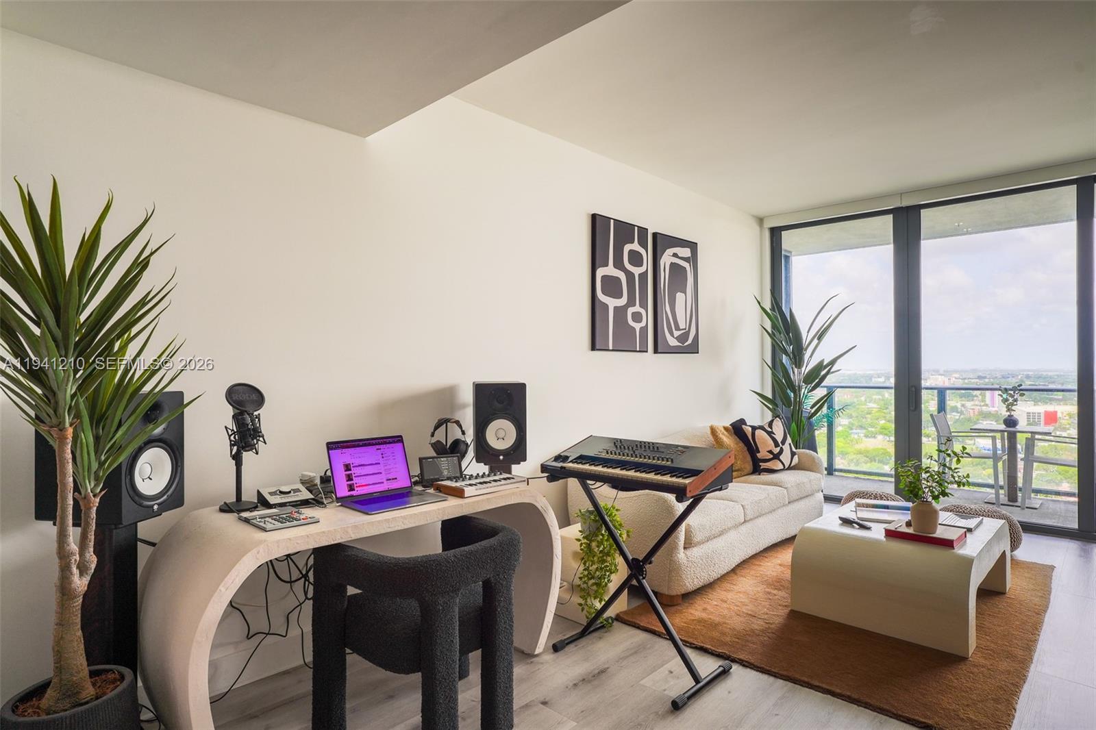 A modern living room features a music production desk, a sofa, and a balcony with views — 121 NE 34th St # 2711, Miami FL 33137, MIAMI, FL