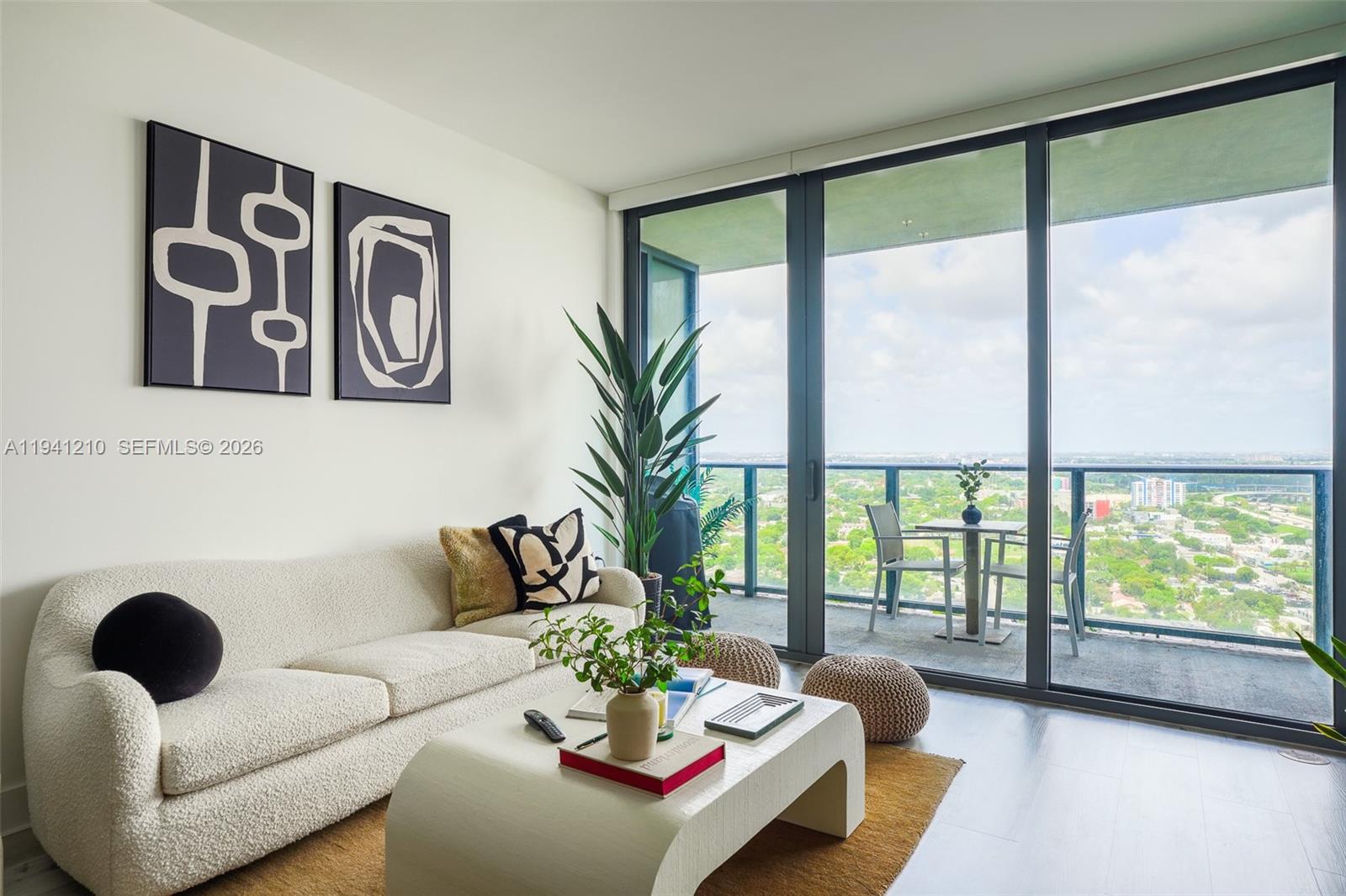 A modern living room features a cream sofa, a coffee table, and a balcony view — 121 NE 34th St # 2711, Miami FL 33137, MIAMI, FL