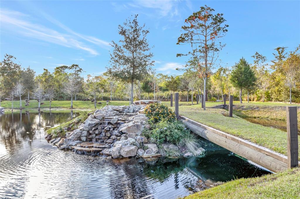 A stone waterfall feature sits in a pond next to a wooden footbridge outdoors — 7330 CRABGRASS ROAD, ST CLOUD, FL