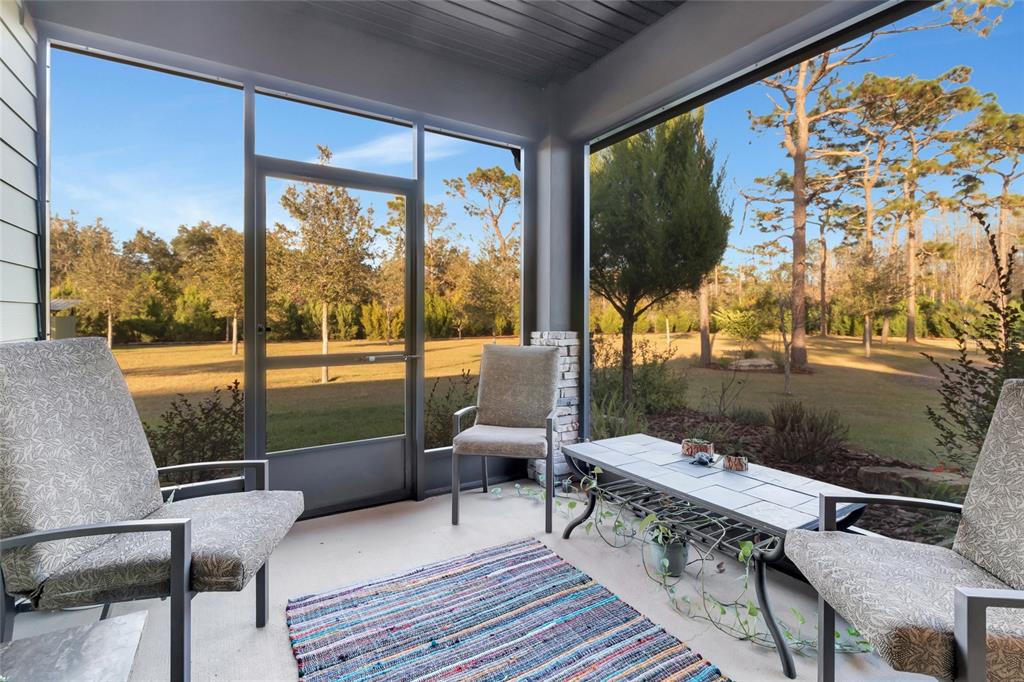 A screened-in porch features three chairs, a tiled table, and a view of trees — 7330 CRABGRASS ROAD, ST CLOUD, FL