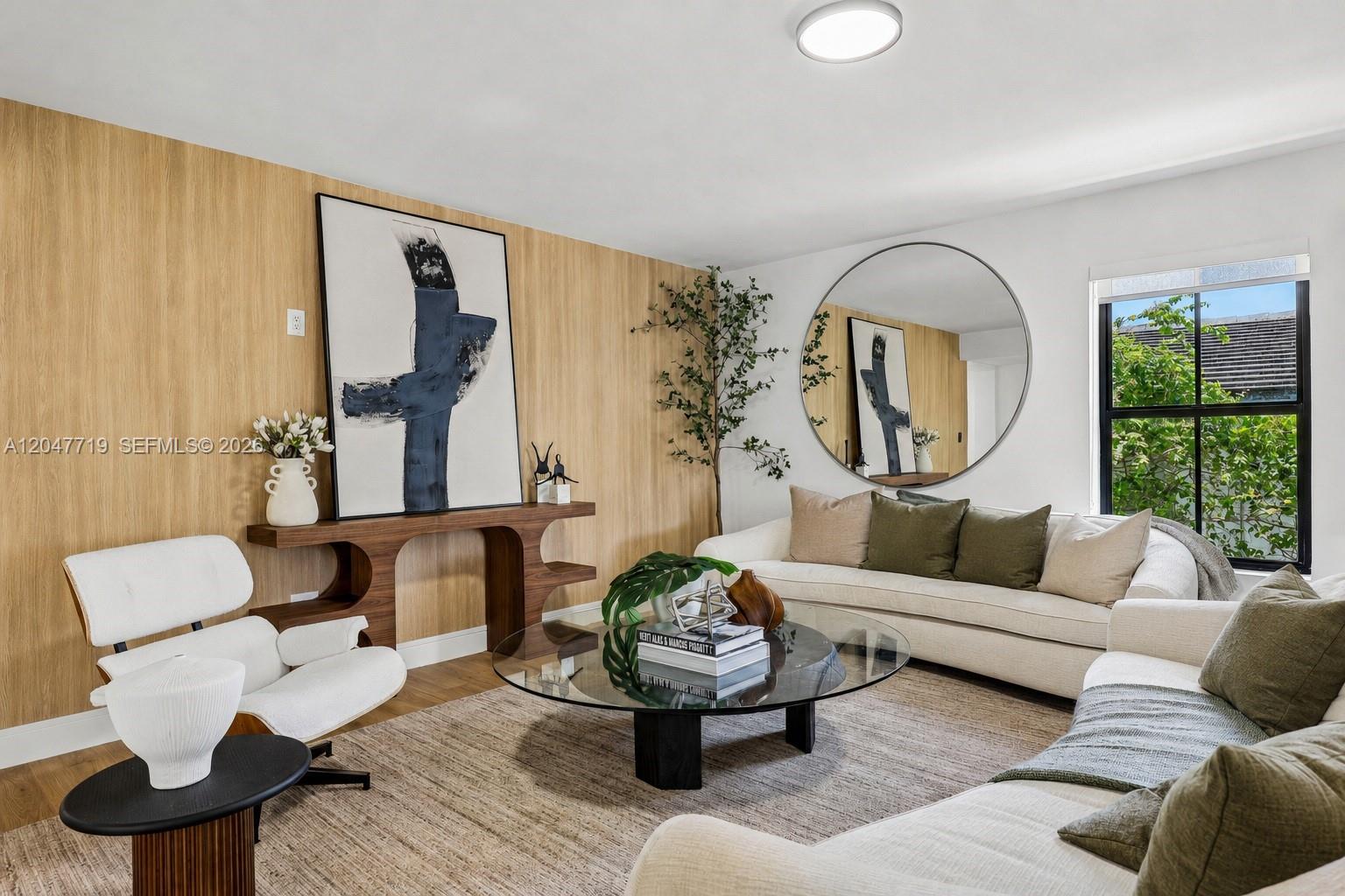 A living room features a wood-paneled wall, a round mirror, and neutral-toned furniture — 7811 Carlyle Ave, Miami Beach FL 33141, MIAMI BEACH, FL