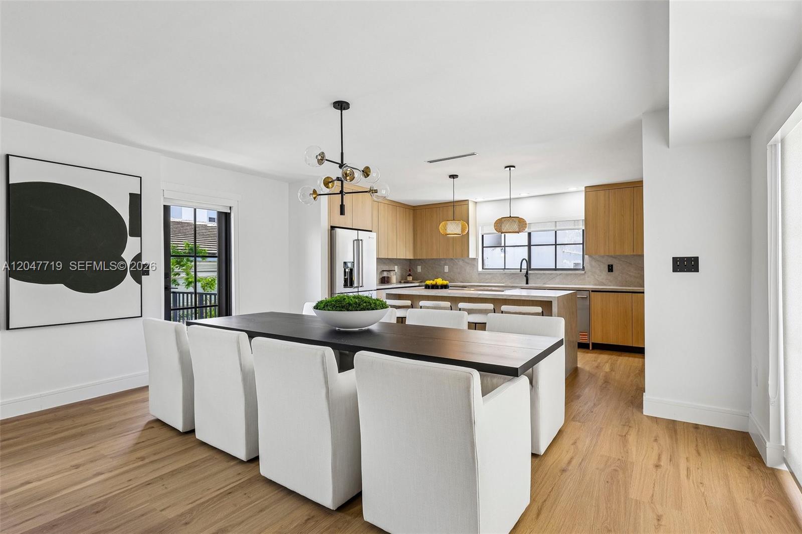 A modern dining area with a dark table and white chairs sits before an open kitchen — 7811 Carlyle Ave, Miami Beach FL 33141, MIAMI BEACH, FL