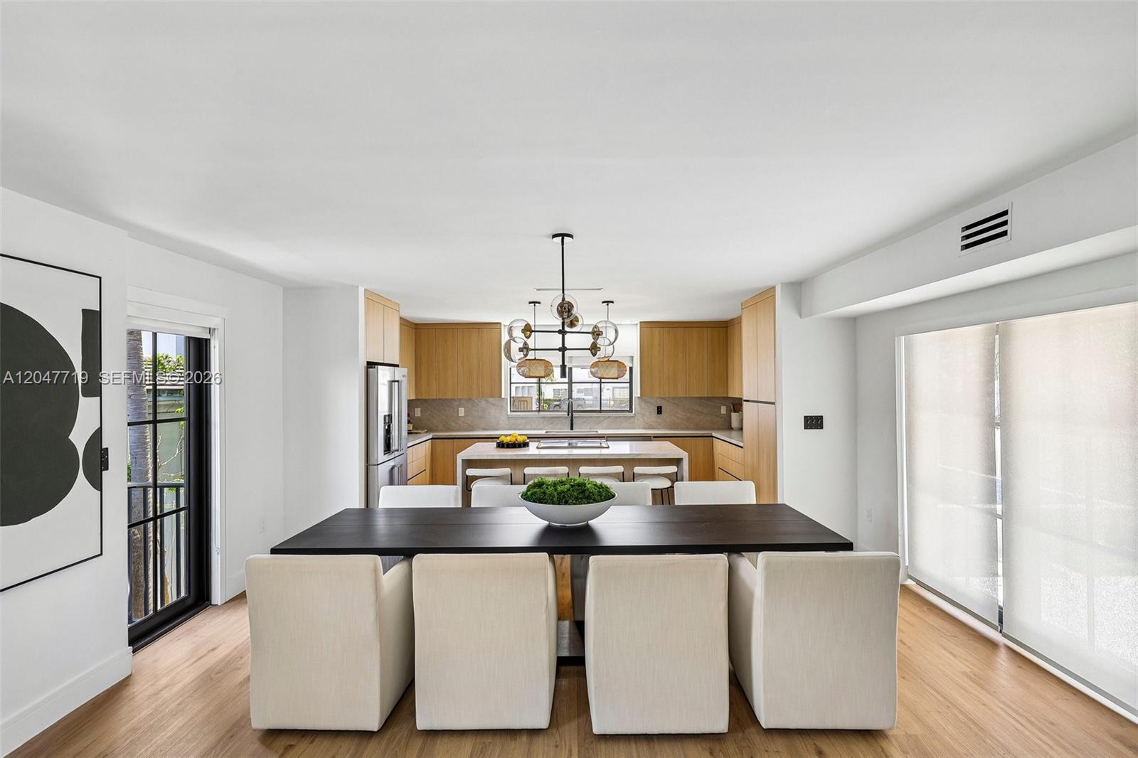 A modern dining area features a dark table, light chairs, and an open-concept kitchen — 7811 Carlyle Ave, Miami Beach FL 33141, MIAMI BEACH, FL