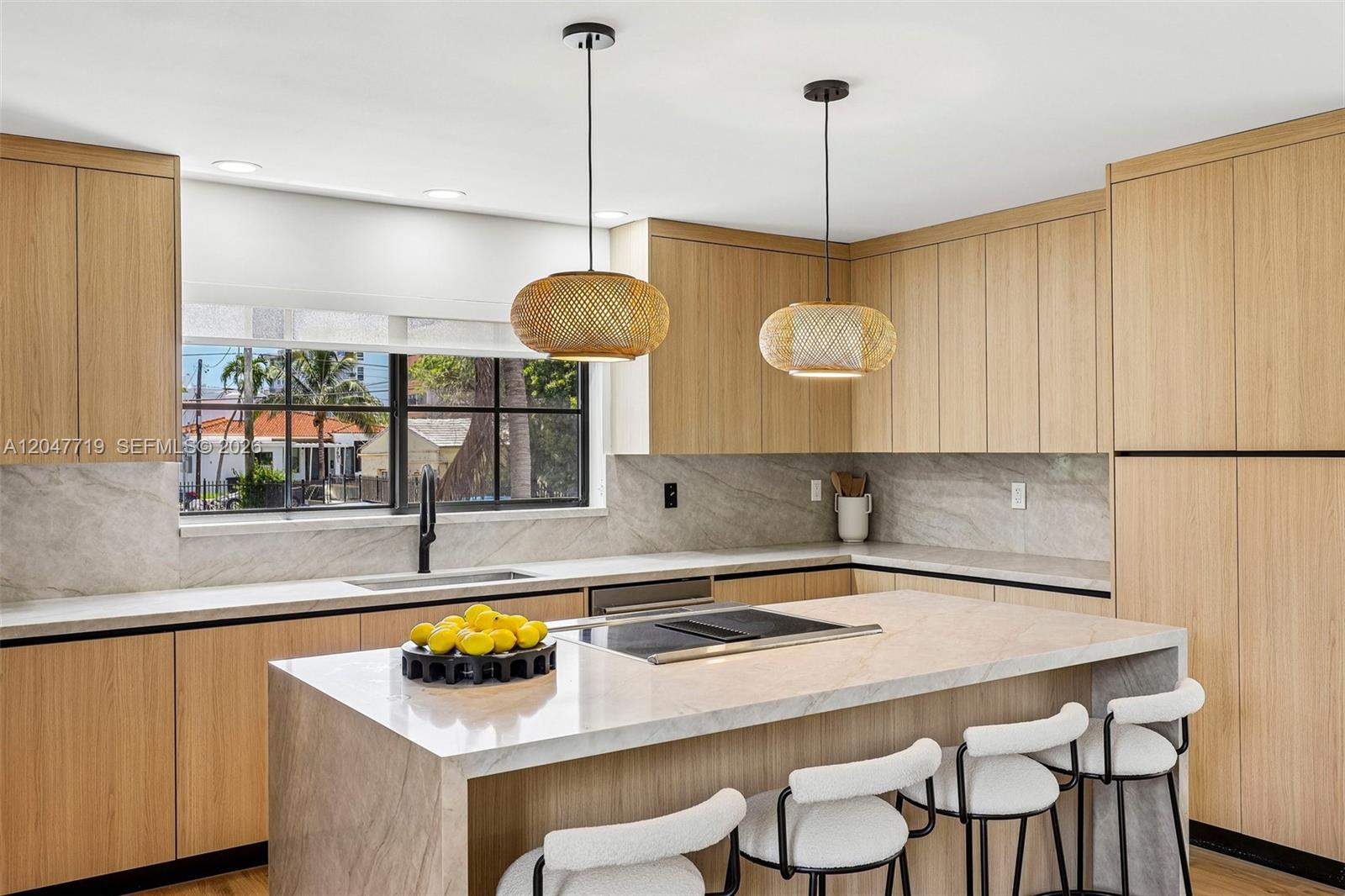 A modern kitchen features light wood cabinetry, stone countertops, and two woven pendant lights — 7811 Carlyle Ave, Miami Beach FL 33141, MIAMI BEACH, FL