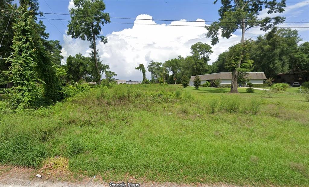 A vacant, grassy lot with scattered trees and shrubs sits next to a residential building — 0 SAND AVENUE, APOPKA, FL