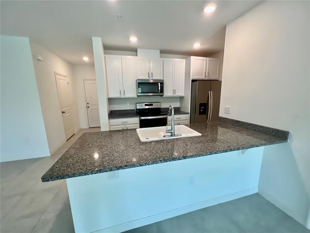 A kitchen with white cabinets, granite countertops, a stainless steel refrigerator, and a breakfast bar — 3805 HAMPTON CHASE LANE, SANFORD, FL