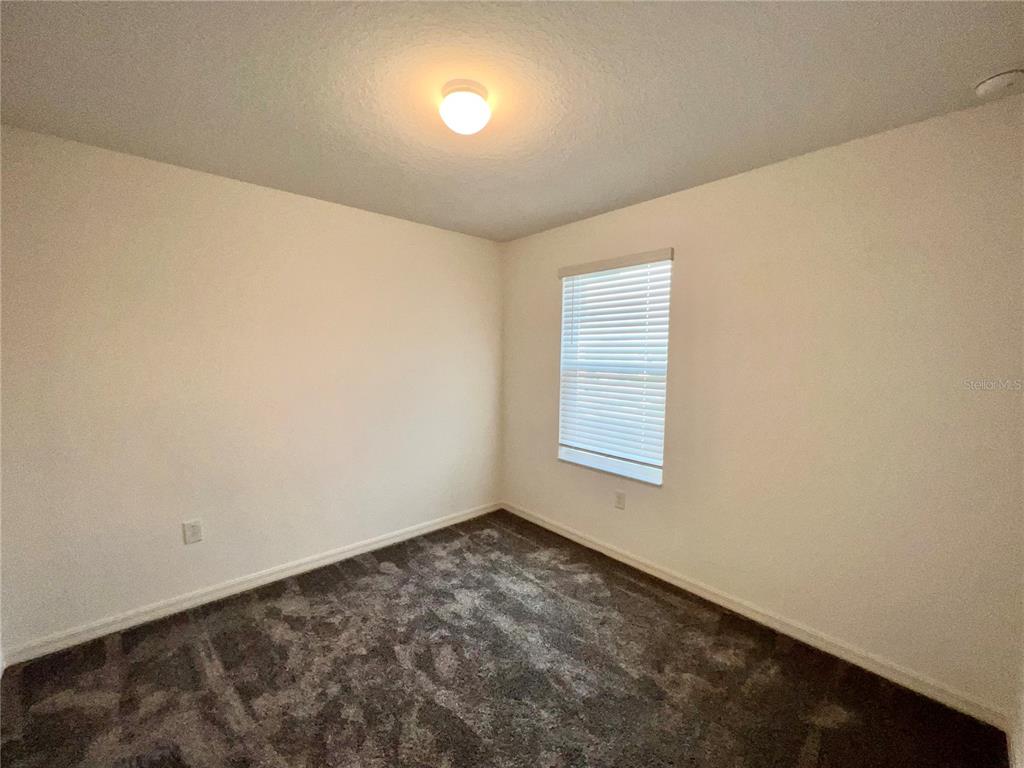 An empty bedroom features beige walls, dark gray carpeting, a single window, and a ceiling light — 3805 HAMPTON CHASE LANE, SANFORD, FL