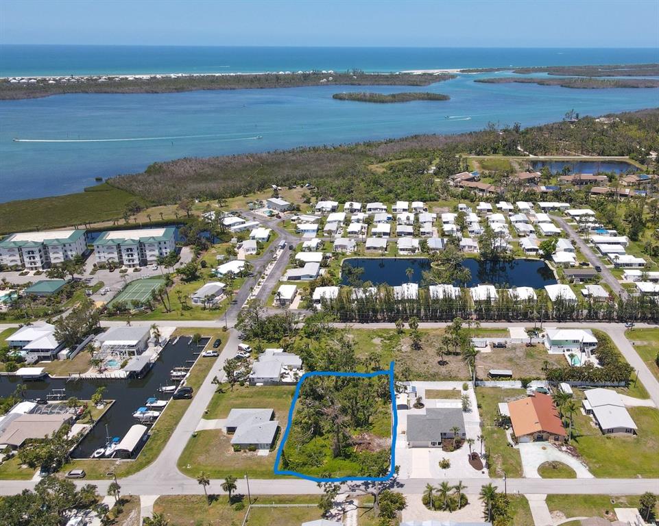 An aerial view shows a vacant, tree-covered residential lot outlined in blue near a canal — 9161 PINE COVE DRIVE, ENGLEWOOD, FL