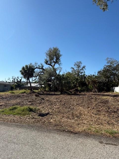A cleared, vacant lot features several mature trees under a clear blue sky — 9161 PINE COVE DRIVE, ENGLEWOOD, FL