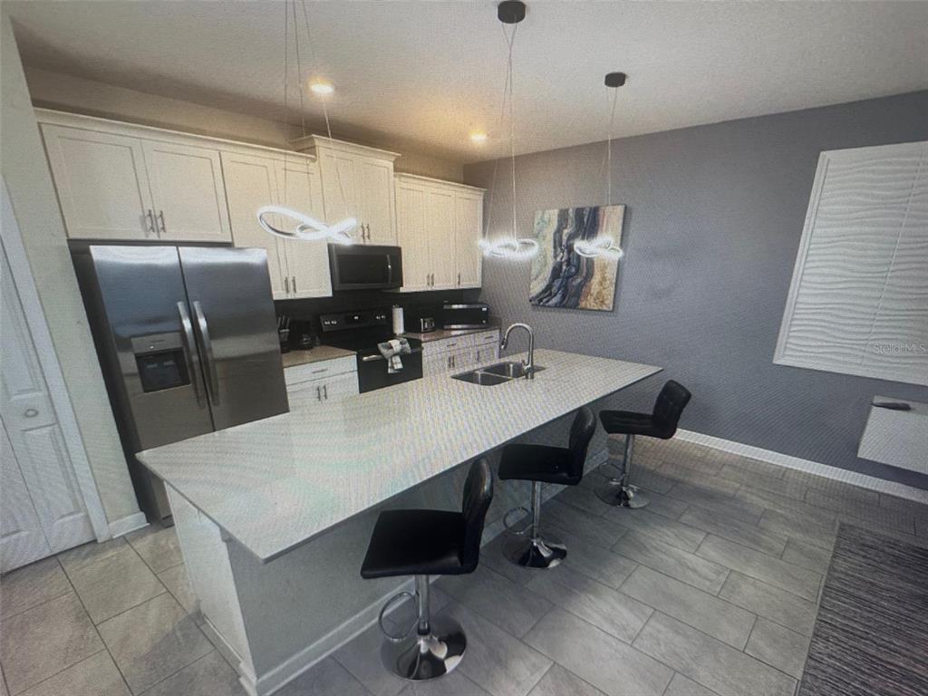A modern kitchen features white cabinetry, stainless steel appliances, a large island, and bar seating — 4976 WINDERMERE AVENUE, KISSIMMEE, FL