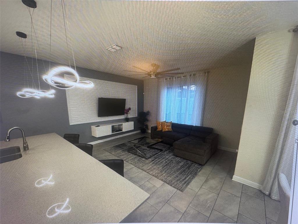 A modern living room with a gray sectional, wall-mounted console, and pendant lights over island — 4976 WINDERMERE AVENUE, KISSIMMEE, FL