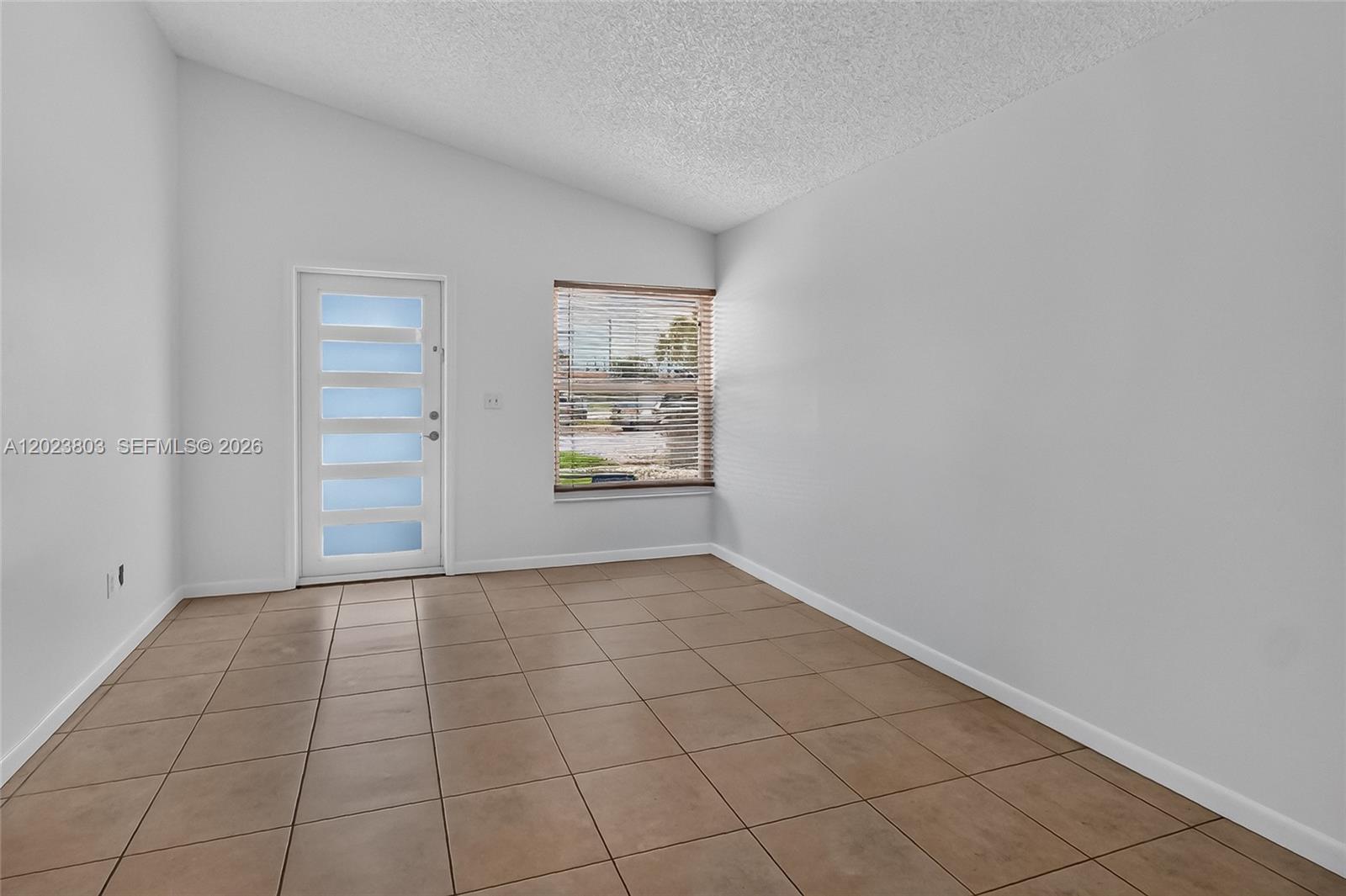 An empty room features white walls, a vaulted ceiling, tiled flooring, and a glass-paneled door — 2514 W 74th St, Hialeah FL 33016, HIALEAH, FL