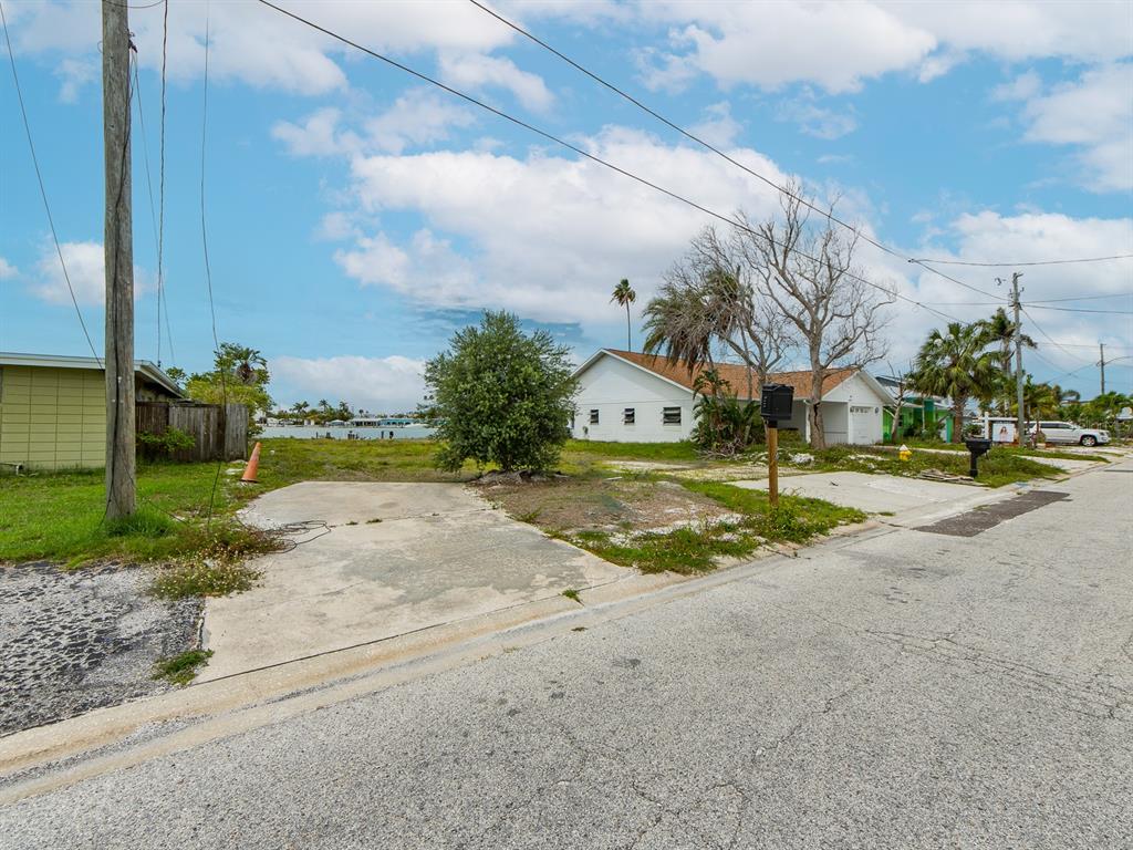 A vacant lot with a concrete driveway sits between two houses near a waterway — 813 BAY POINT DRIVE, MADEIRA BEACH, FL