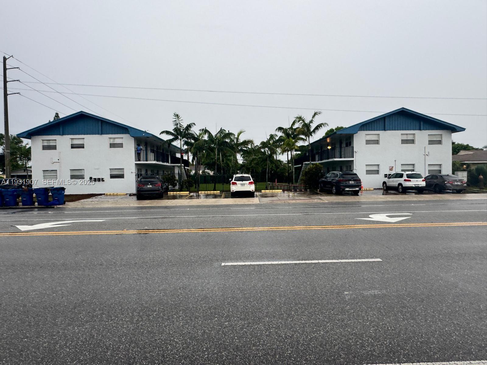 Two white two-story apartment buildings face each other across a parking lot by a road — 215 W Blue Heron Blvd, Riviera Beach FL 33404, RIVIERA BEACH, FL