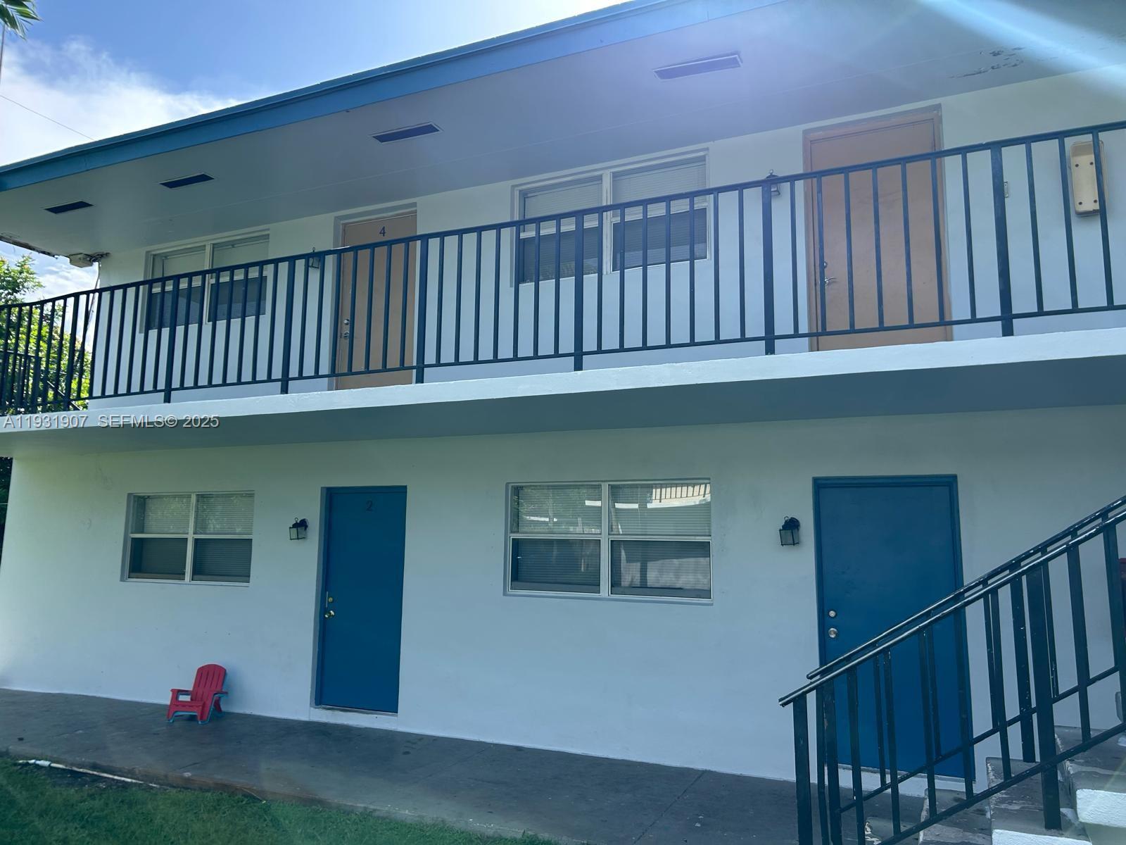 A two-story apartment building features blue doors, white exterior walls, and black metal railings — 215 W Blue Heron Blvd, Riviera Beach FL 33404, RIVIERA BEACH, FL