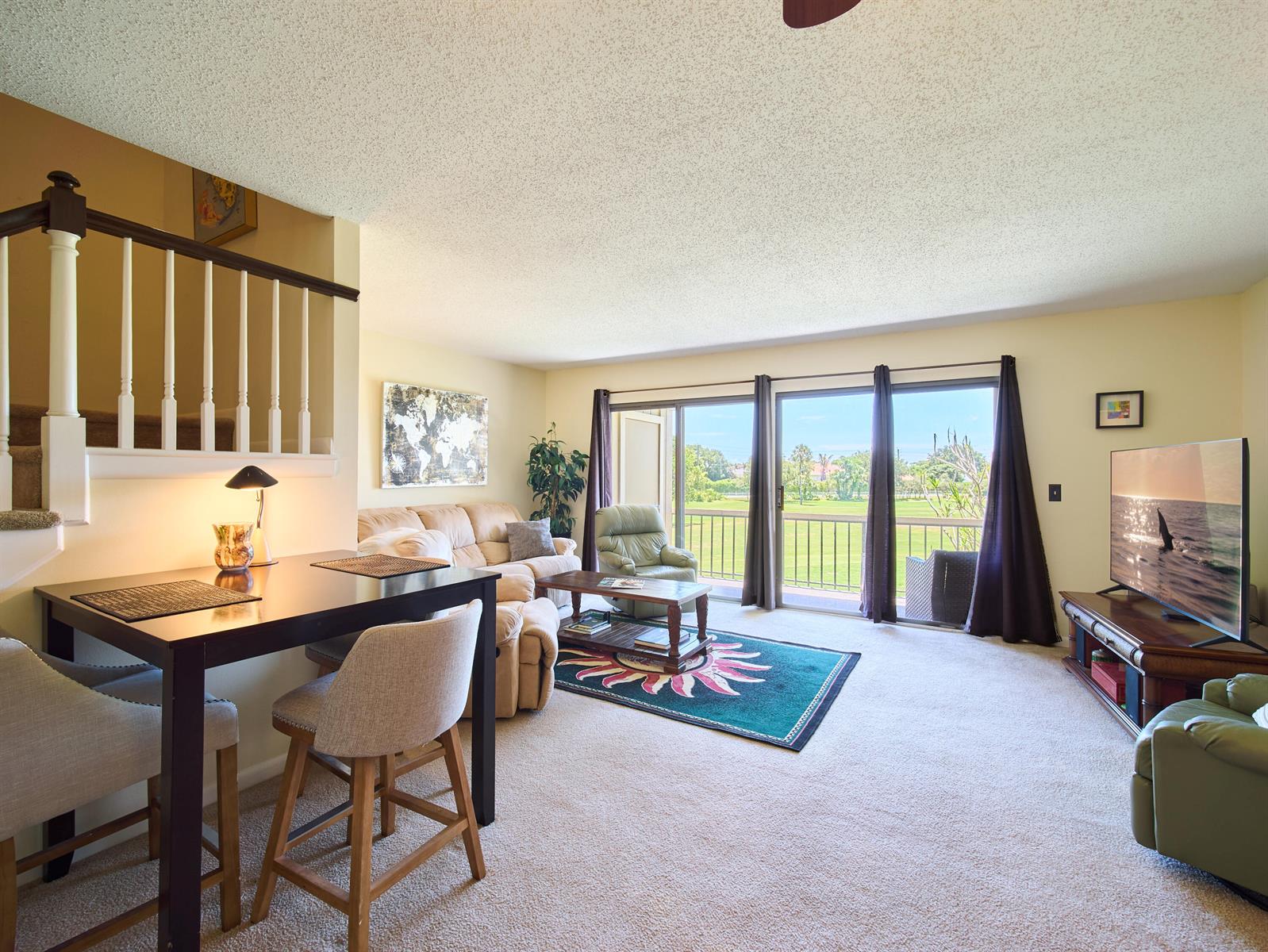 A living room with a dining area, beige carpeting, and sliding glass doors to a balcony — 18439 SE Wood Haven Lane # M, Jupiter FL 33469, JUPITER, FL