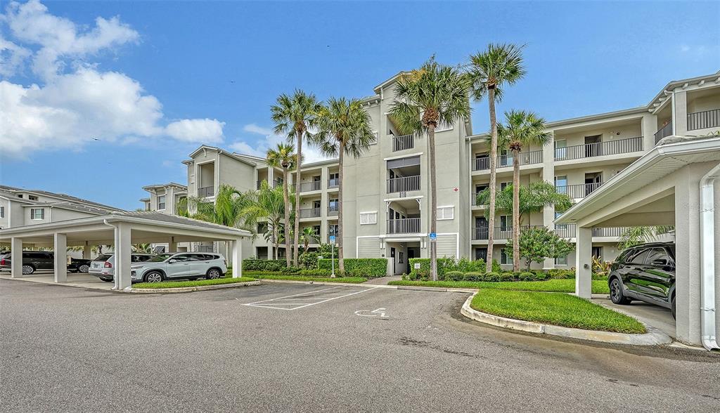 A multi-story apartment building with covered parking and palm trees in a sunny parking lot — 910 TIDEWATER SHORES LOOP UNIT 402, BRADENTON, FL